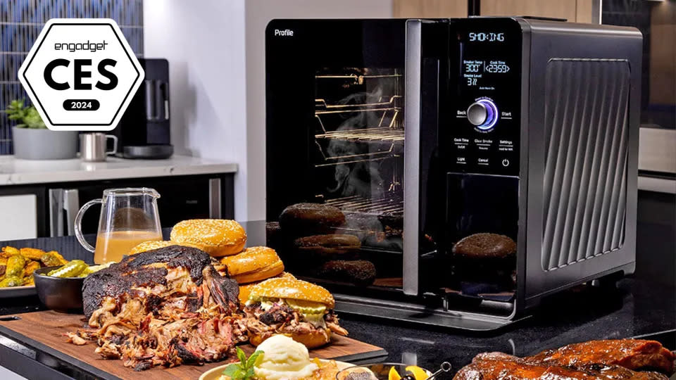 Una imagen con una insignia de Engadget Best of CES 2024 que muestra el producto: GE Profile Smart Indoor Smoker en una isla de cocina abarrotada de gente rodeada de pilas de pechuga y panecillos de hamburguesa. (GE)