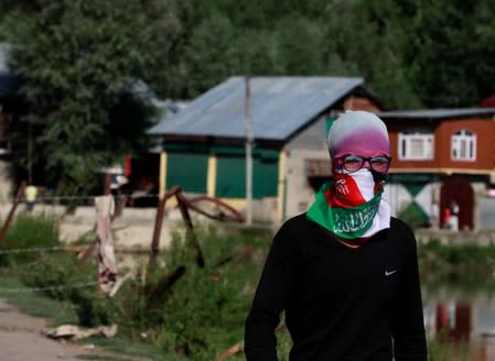 A Kashmiri masked protester stands near a barricade to block the entrance of a neighbourhood, during restrictions after the scrapping of the special constitutional status for Kashmir by the government, in Srinagar