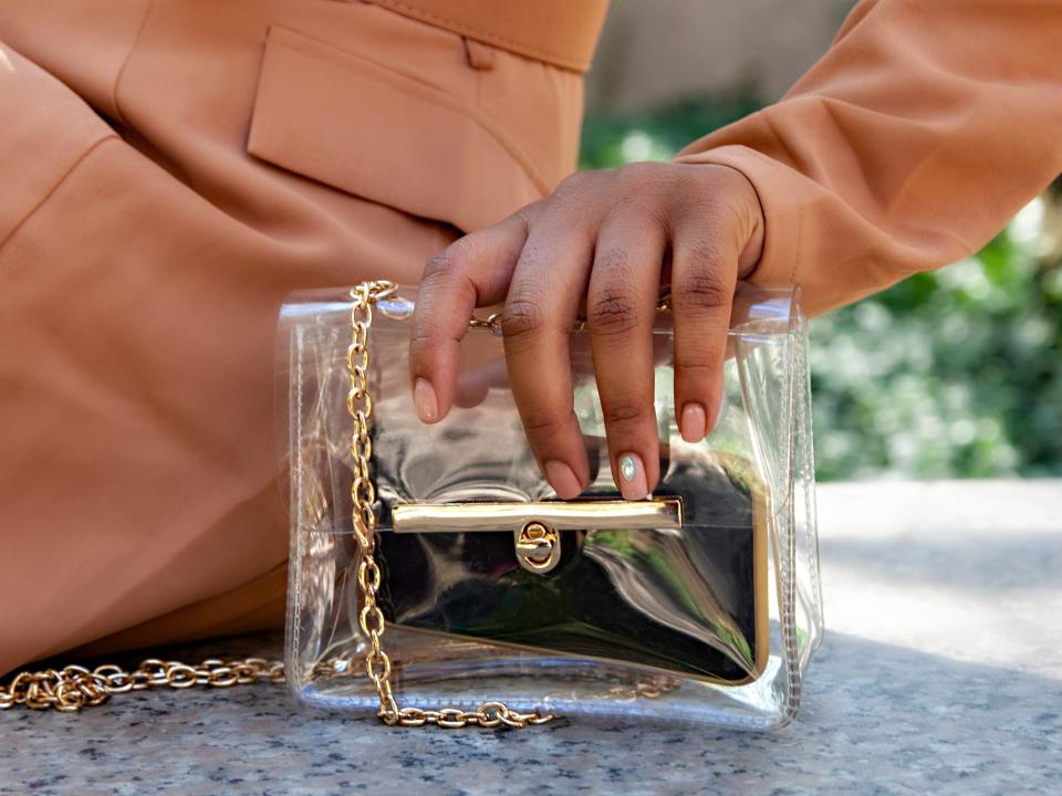 person wearing trench coat and holding a clear plastic-looking purse with gold details