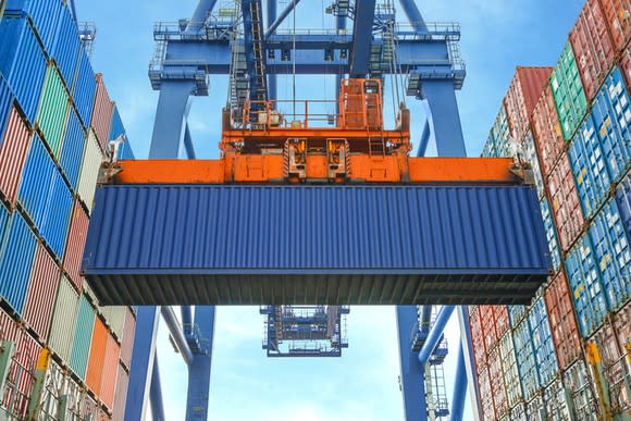 A blue container, surrounded on both sides by stacked containers in varying colors, being lifted at port.