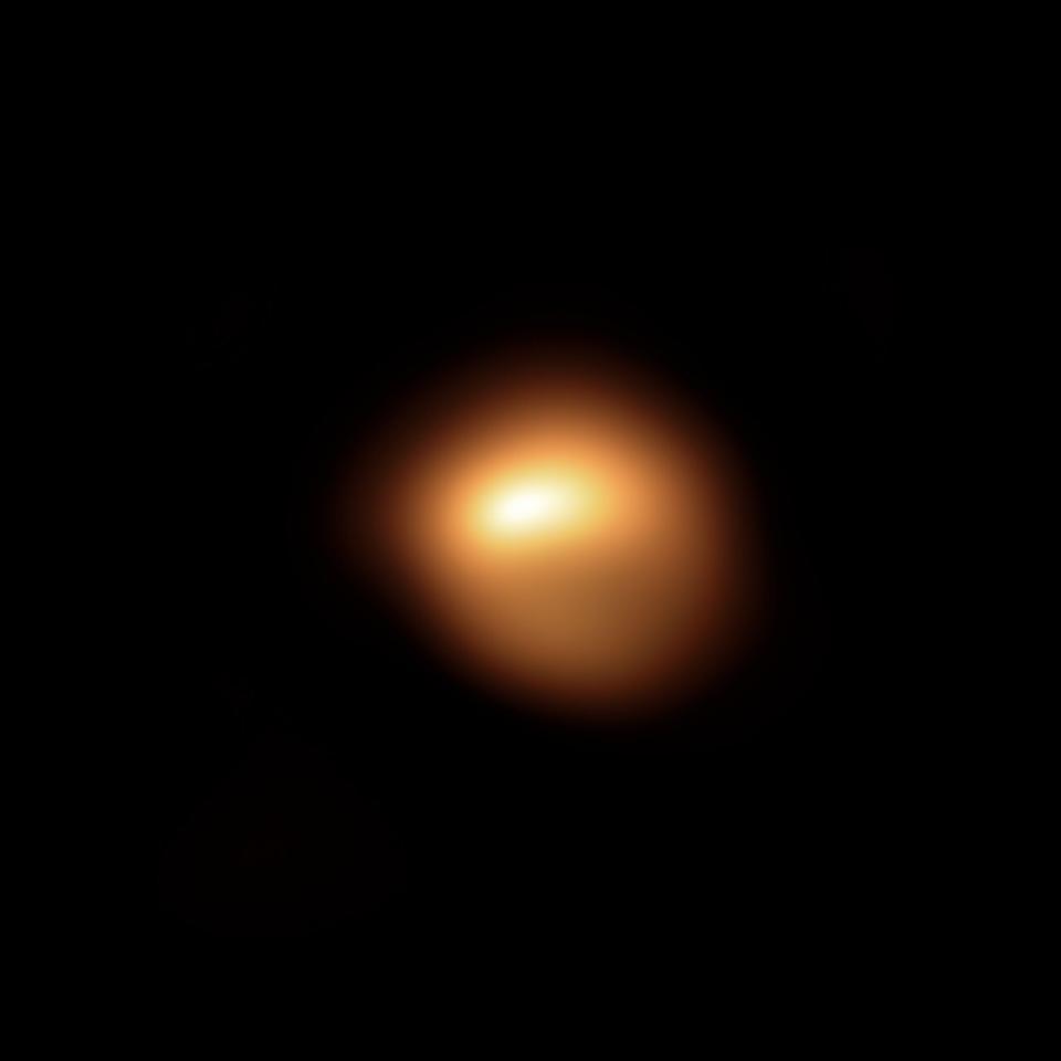 An asymmetrical, blurry sphere sits in the center of a black background. Its face is smeared with dull shades of yellow and pale brown.