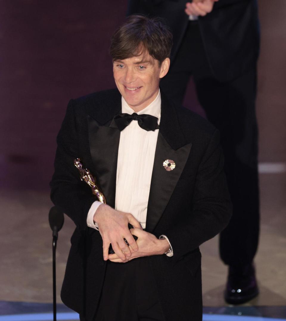 Cillian Murphy in a black tuxedo cradles an Oscar statuette onstage.