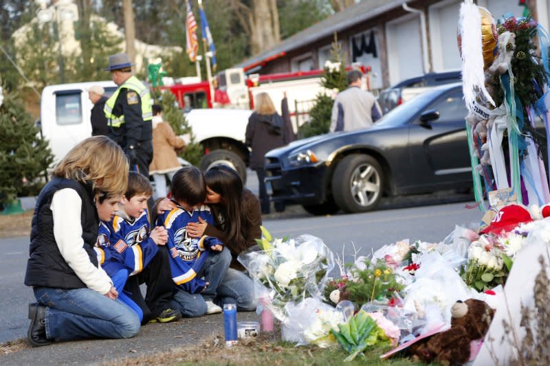 Mourners gather near a memorial filled with flowers, stuffed toys and candles at the entrance to Sandy Hook Elementary School in Newtown, Conn., following a shooting December 14, 2012. File Photo by John Angelillo/UPI