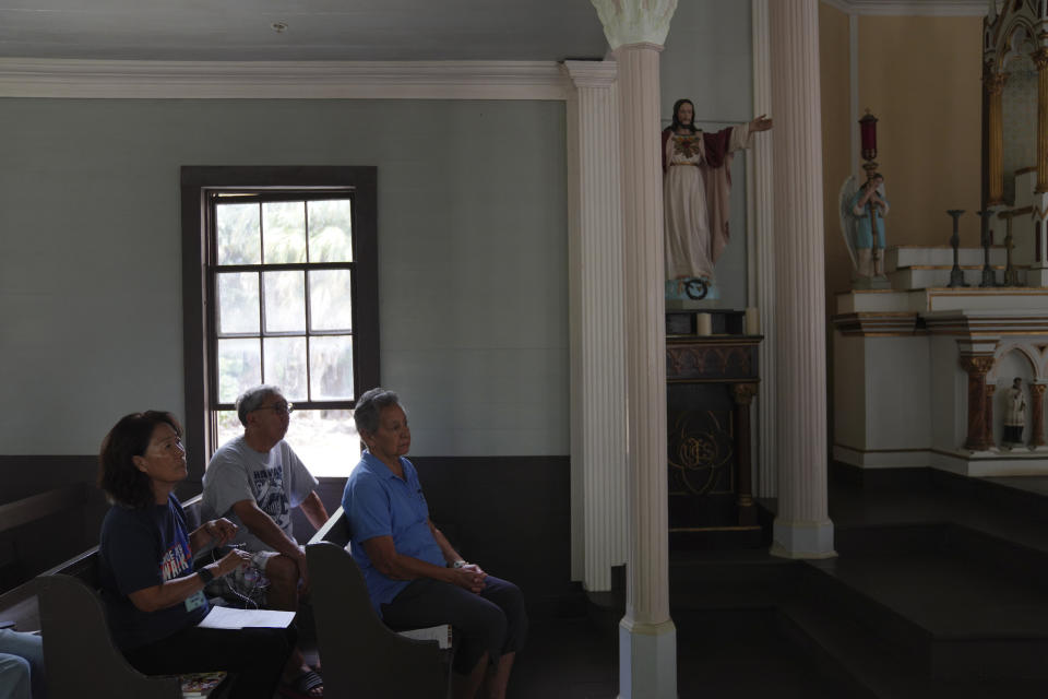 Kyong Son Toyofuku, left, her husband, Lance Toyofuku, center, and sister Alicia Damien Lau, celebrate Mass at St. Philomena Church during a pilgrimage tour of Kalaupapa, Hawaii, on Tuesday, July 18, 2023. The church was expanded and used by St. Damien and his parishioners in the 1800s while he lived with and cared for leprosy patients banished to Kalaupapa. (AP Photo/Jessie Wardarski)