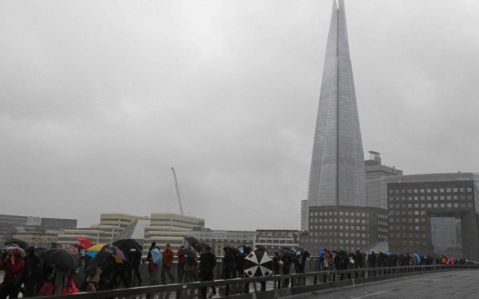 Commuters walk in the rain past a security barrier installed between the pavement and the road on London Bridge - Credit: JUSTIN TALLIS/AFP/Getty Images