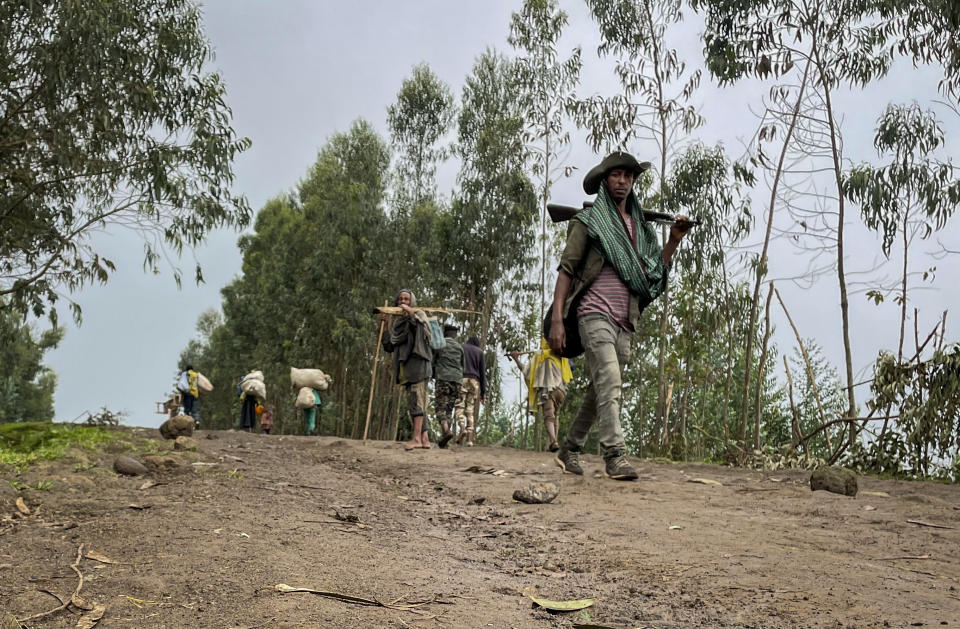 An unidentified armed militia fighter walks down a path as villagers flee with their belongings in the other direction, near the village of Chenna Teklehaymanot, in the Amhara region of northern Ethiopia Thursday, Sept. 9, 2021. At the scene of one of the deadliest battles of Ethiopia's 10-month Tigray conflict, witness accounts reflected the blurring line between combatant and civilian after the federal government urged all capable citizens to stop Tigray forces "once and for all." (AP Photo)