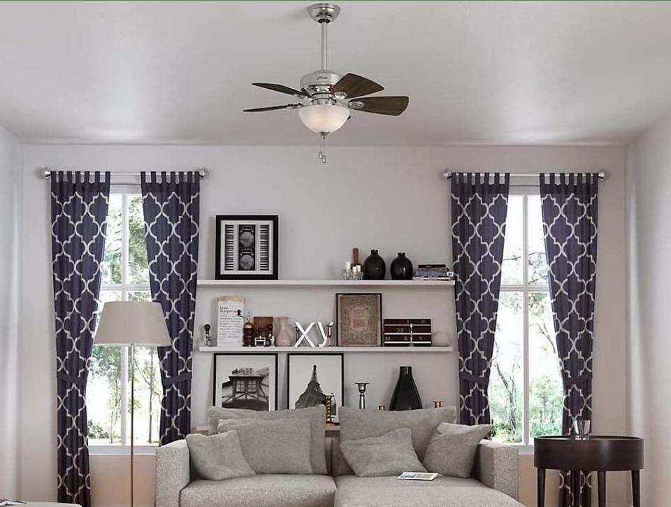 Blue patterned grommet curtains in a high-ceilinged living room with grey sofa.