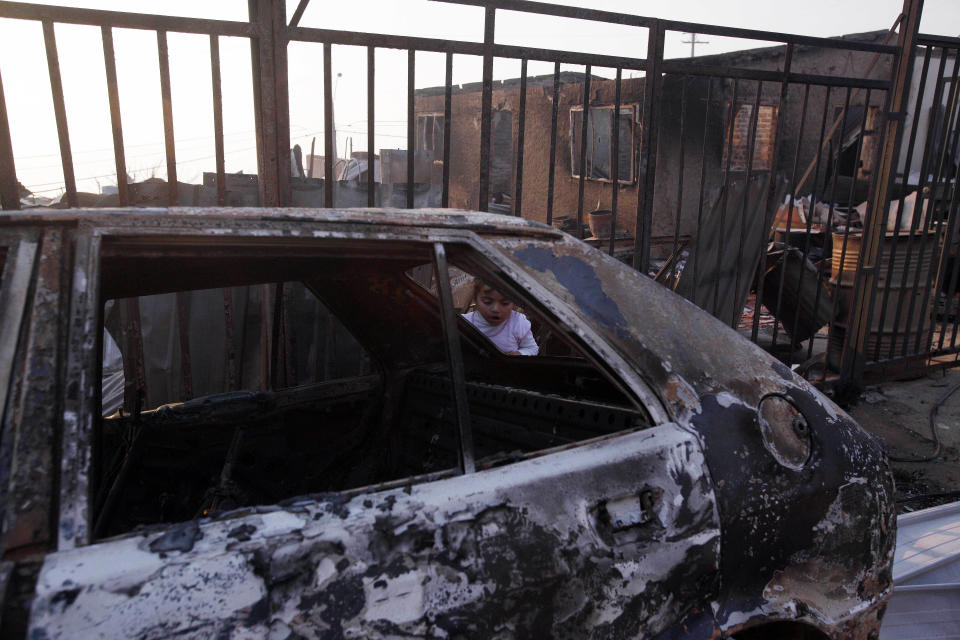 A young girl looks at the charred remains of a vehicle after a large forest fire reached urban areas in Valparaiso, Chile, Sunday April 13, 2014. Authorities say the fires have destroyed hundreds of homes, forced the evacuation of thousands and claimed the lives of at least seven people. ( AP Photo/ Luis Hidalgo)