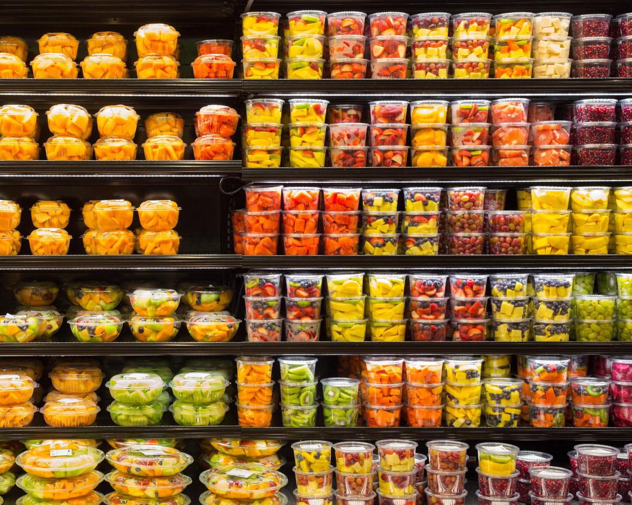 Six rows of a selection of packaged cut fruits in the refrigerated area at a grocery store, very colorful, black shelves