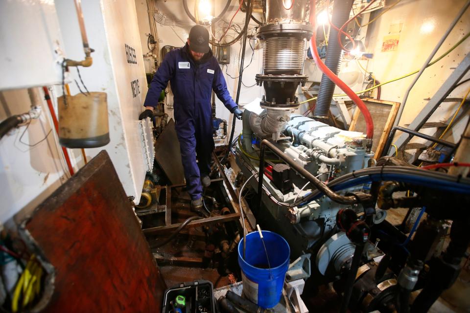 Windward Power Systems technician Jack Benway walks across the exposed hull of the fishing boat Fisherman as he works on the cooling system of the new engine they have installed aboard the New Bedford fishing boat.