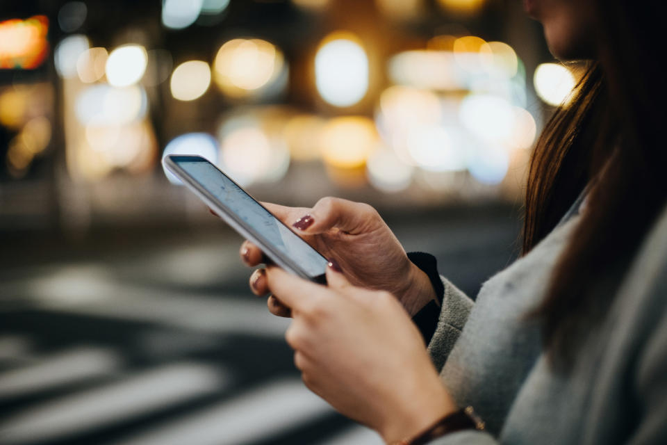 A woman holds her cell phone, which displays a map with her location