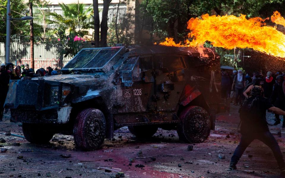 Demonstrators set a riot police vehicle on fire during clashes on the commemoration of the first anniversary of the social uprising in Chile - AFP