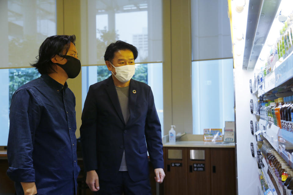 Telexistence CEO Jin Tomioka, left, and FamilyMart Executive Officer Tomohiro Kano look at shelves of a FamilyMart convenience store in Tokyo, Friday, Aug. 26, 2022, as the TX SCARA robot stocks shelves with battles and cans. The robot can restock shelves with up to 1,000 bottles and cans a day. (AP Photo/Yuri Kageyama)