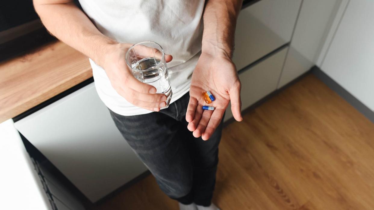 the guy holds vitamins and pills in his hand in the kitchen modern cuisine water young guy casual style glass of water