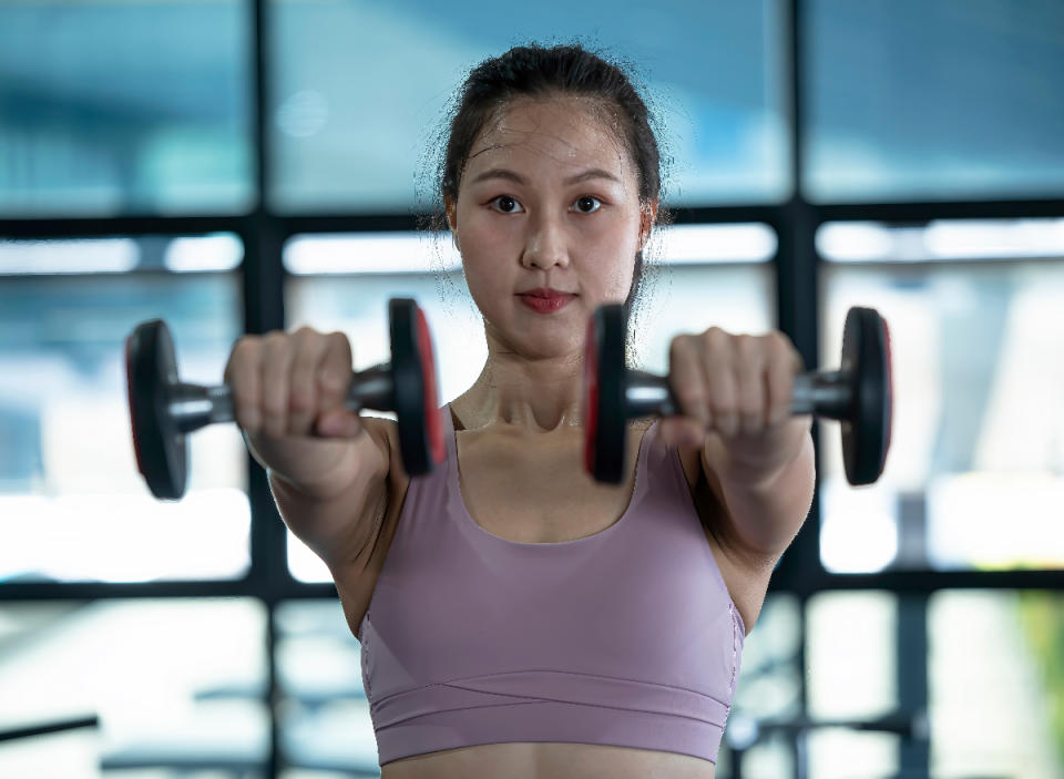 fitness woman doing dumbbell front raises at the gym