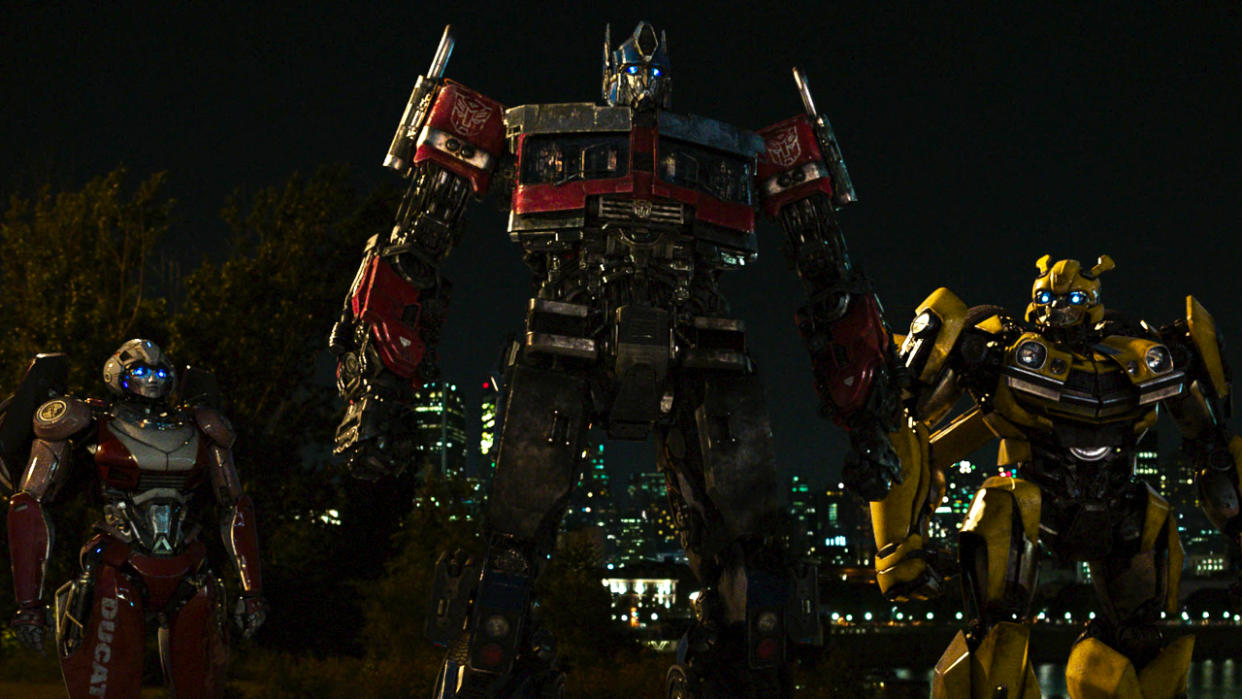  Optimus Prime stands with Arcee and Bumblebee in a night scene in Transformers: Rise of the Beasts. 