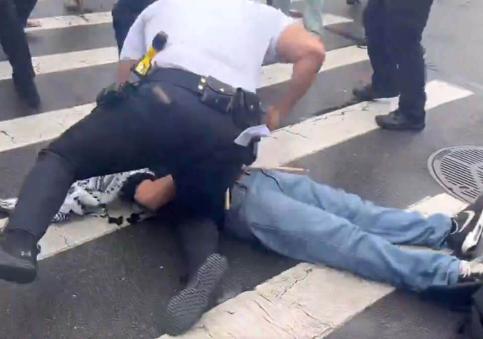 A New York Police Department officer pictured punching an anti-war demonstrator during a protest in Brooklyn on 18 March (Katie Smith)