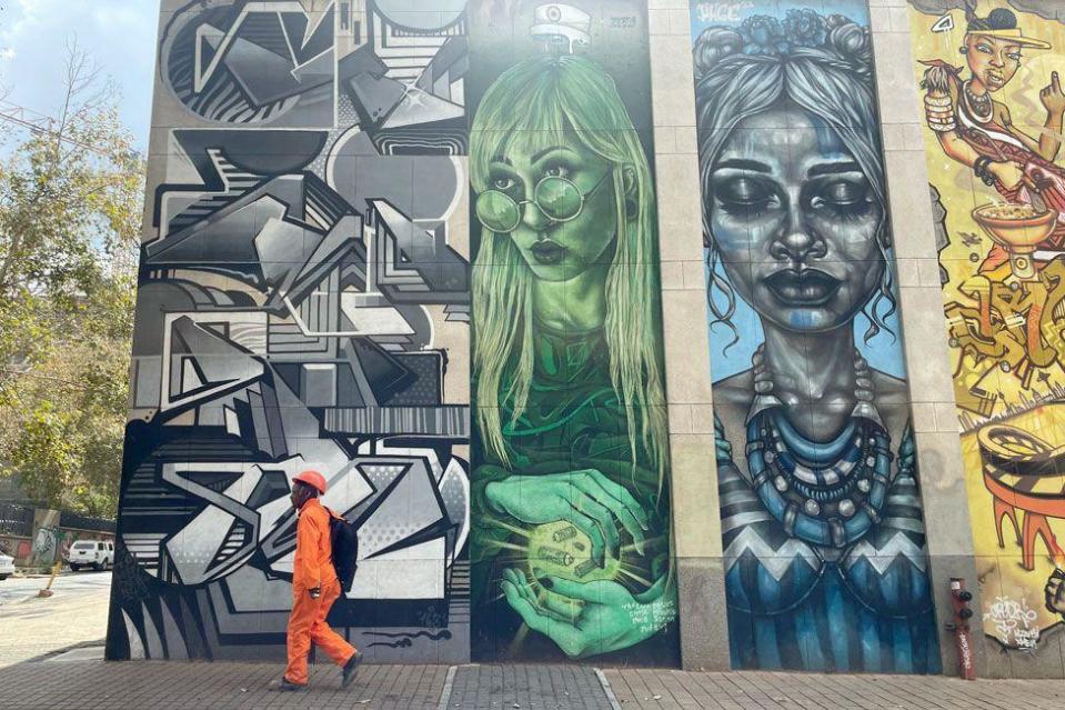 A man walking past mural portraits in Braamfontein, Johannesburg