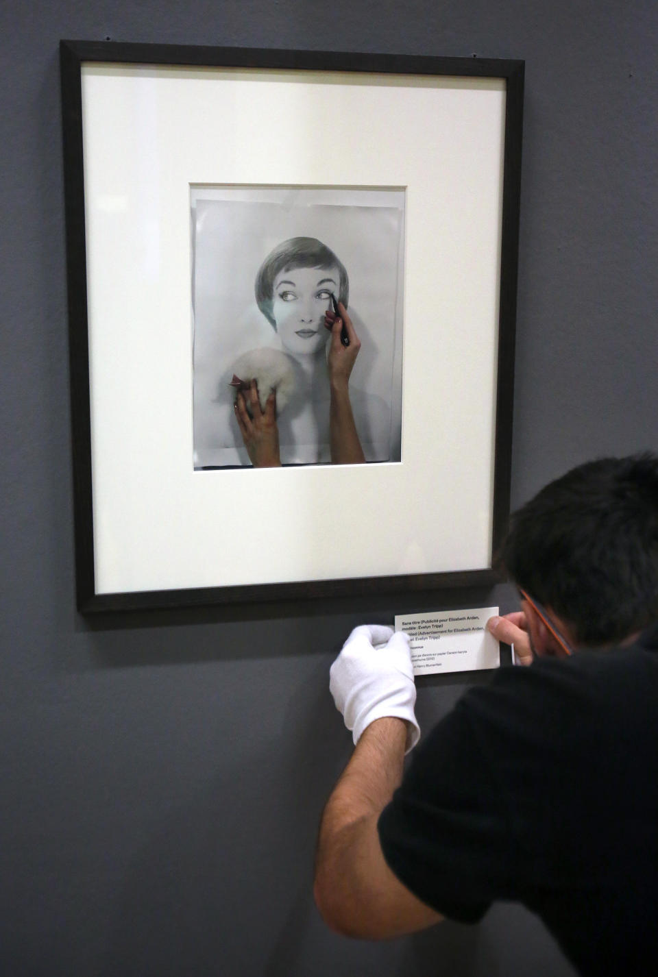 An employee adjusts a label under a photo by German-born American photographer Erwin Blumenfeld during the preparation of an exhibition to be held from Oct. 15 to Jan. 26, 2014, at the Jeu de Paume museum in Paris, Friday Oct. 11, 2013. Sign reads: Untitled (Advertisment for Elizabeth Arden, model: Evelyn Tripp).(AP Photo/Remy de la Mauviniere)