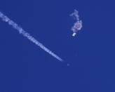 In this photo provided by Chad Fish, the remnants of a large balloon drift above the Atlantic Ocean, just off the coast of South Carolina, with a fighter jet and its contrail seen below it, Saturday, Feb. 4, 2023. The downing of the suspected Chinese spy balloon by a missile from an F-22 fighter jet created a spectacle over one of the state’s tourism hubs and drew crowds reacting with a mixture of bewildered gazing, distress and cheering. (Chad Fish via AP)