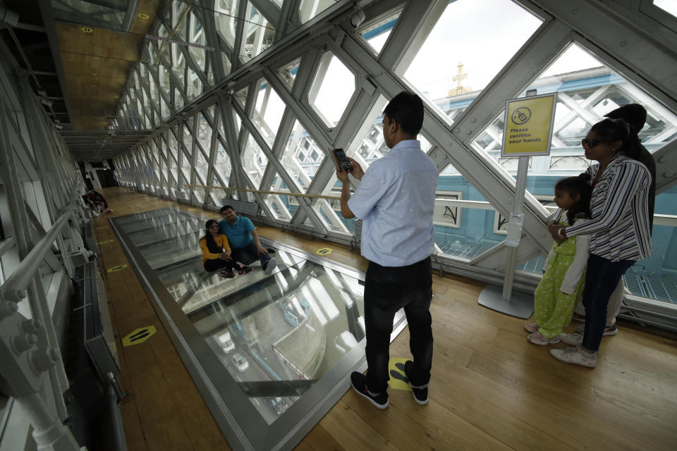 Visitors pose for photographs on the glass walkway at the Tower Bridge Visitor Attraction, in London, on the first day it was allowed to reopen as the British government relaxes its third coronavirus lockdown restrictions, Monday, May 17, 2021. (AP Photo/Matt Dunham)