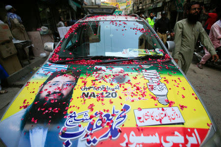 A resident walks past a parked car, decorated with a poster of Mohammad Yaqoob Sheikh, nominated candidate of political party, Milli Muslim League (MML), during an election campaign for the National Assembly NA-120 constituency in Lahore, Pakistan September 9, 2017. Picture taken September 9, 2017. REUTERS/Mohsin Raza