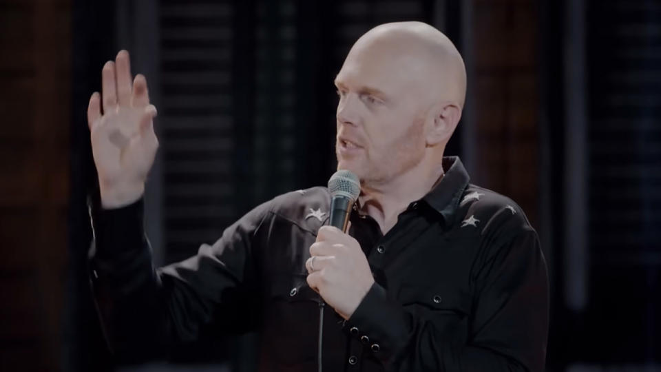 Bill Burr holding his right hand up, making a joke.