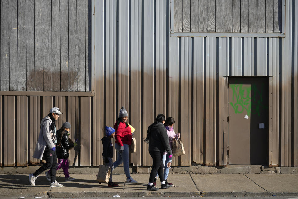 Immigrants walk down the sidewalk outside a shelter in the Pilsen neighborhood of Chicago, after receiving some items Tuesday, Dec. 19, 2023. The death of a 5-year-old migrant boy and reported illnesses in other children living at the shelter has raised concerns about the living conditions and medical care provided for asylum-seekers arriving in Chicago. Four more people living in the same shelter — mostly children — were hospitalized with fevers this week. (AP Photo/Charles Rex Arbogast)