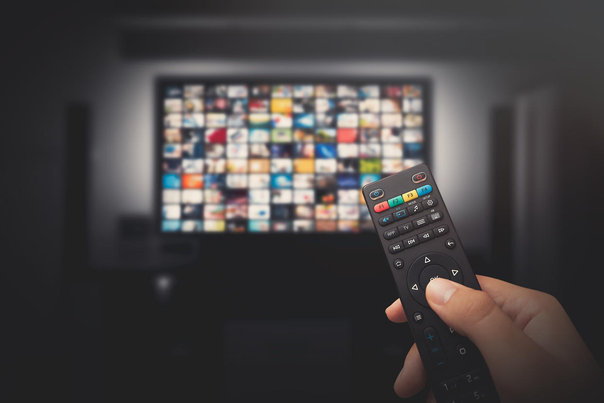 Multimedia video concept on TV set in dark room. Man watching TV with remote control in hand.