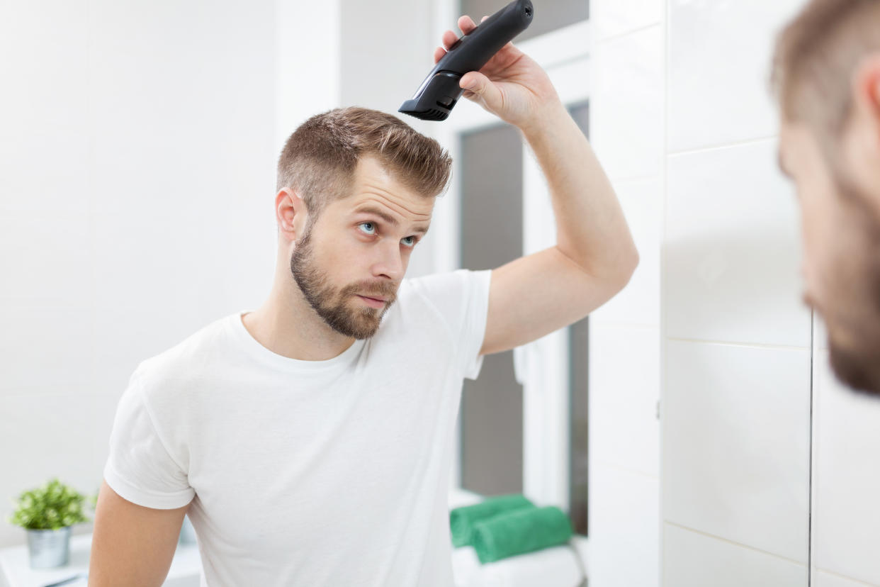 Handsome bearded man cutting his own hair with a clipper