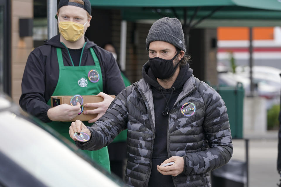 Former Seattle Sounders MLS soccer player Brad Evans, right, hands out stickers that read "Voted" to customers as he takes part in a get-out-the-vote event at a Starbucks store, Tuesday, Oct. 27, 2020, in Seattle's White Center neighborhood. Washington is a vote by mail state, and thousands of ballots have already been mailed back, dropped off in boxes, or cast in person. (AP Photo/Ted S. Warren)