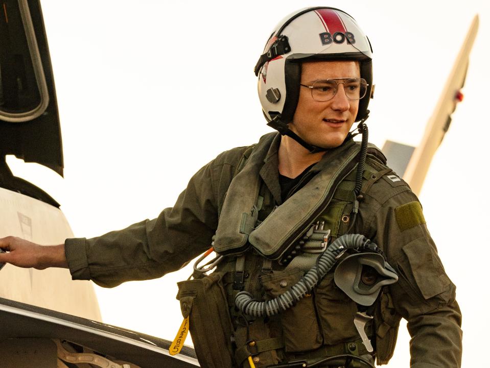 Lewis Pullman in pilot uniform climbing into jet cockpit