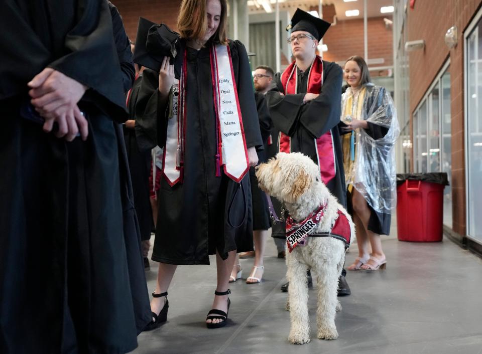 May 7, 2023; Columbus, Ohio, United States; Kaylee Clark of Miamisburg waits in the RPAC with Springer, a Goldendoodle training with 4 Paws For Ability, before the Ohio State University's spring commencement at Ohio Stadium. Clark's stole displayed the names of all of the dogs she has raised for the program. Mandatory Credit: Barbara Perenic/The Columbus Dispatch