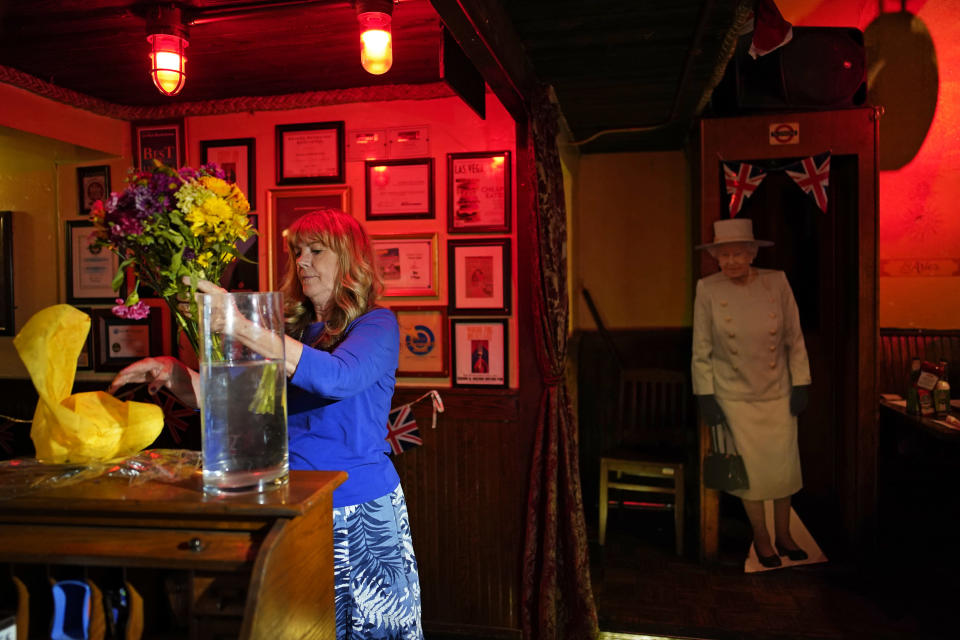Crown & Anchor British Pub manager June LeMay puts flowers in water beside a cardboard cutout of Queen Elizabeth II following her death, Thursday, Sept. 8, 2022, in Las Vegas. (AP Photo/John Locher)
