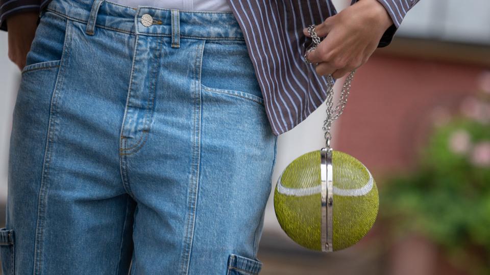 Lois Schindeler wears blue jeans, white underwear, a blue striped shirt, and a tennis ball imitation round bag decorated with crystals outside Baum and Pferdgarten during the Copenhagen Fashion Week Spring/Summer 2024 
