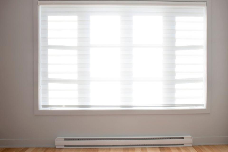 Baseboard heating is seen in a room beneath a large window.