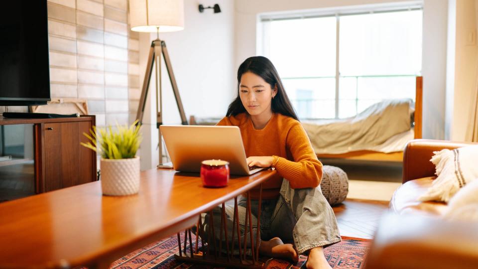 A young woman is using a laptop comfortably in the living room at home.