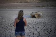 FILE - Misha McBride looks at a formerly sunken boat now on cracked earth hundreds of feet from what is now the shoreline on Lake Mead at the Lake Mead National Recreation Area, Monday, May 9, 2022, near Boulder City, Nev. The sight of fountains, swimming pools, gardens and golf courses in Western cities like Phoenix, Los Angeles, Las Vegas, San Diego and Albuquerque can seem jarring with drought and climate change tightening their grip on the region. But Western water experts say they aren’t necessarily cause for concern. Many Western cities over the past three decades have diversified their water sources, boosted local supplies, and use water more efficiently now than in the past. (AP Photo/John Locher, File)