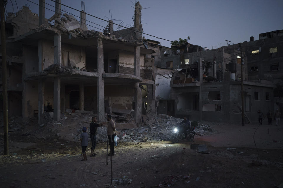 A man rides his motorcycle at night on Al-Baali Street as Palestinians stand next to homes heavily damaged by airstrikes in Beit Hanoun, northern Gaza Strip, Friday, June 11, 2021. (AP Photo/Felipe Dana)