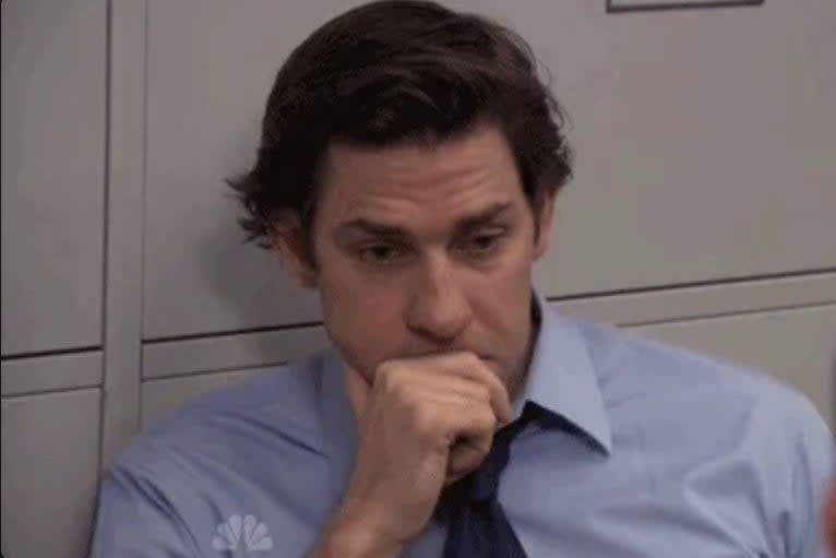 John Krasinski, in business attire, thoughtfully rests his chin on his hand while looking at someone off-screen