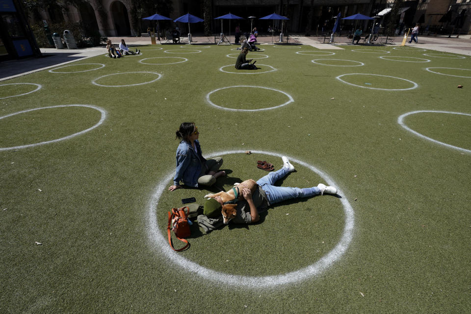 FILE - Kyree Kayoshi, his dog Kumi, and Miranda De Llano use circles marked for social distancing to help battle the COVID-19 virus as they relax at the Pearl Brewery, March 3, 2021, in San Antonio. The U.S. death toll from COVID-19 has hit 1 million, less than 2 1/2 years into the outbreak. (AP Photo/Eric Gay, File)