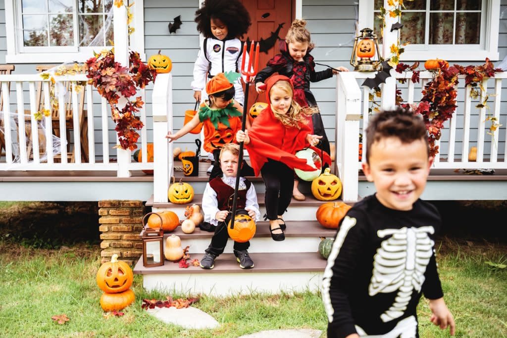 A group of children dressed in costumes go trick-or-treating. 