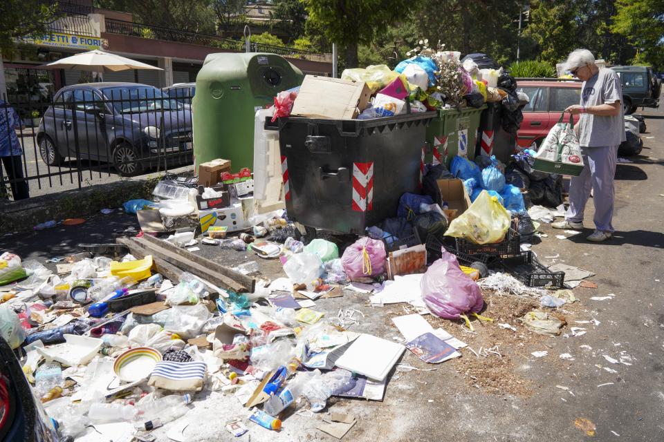 In this photo taken on Monday, June 24, 2019, a man stands by uncollected garbage in Rome. Doctors in Rome are warning of possible health hazards caused by overflowing trash bins in the city streets, as the Italian capital struggles with a renewed garbage emergency aggravated by the summer heat. (AP Photo/Andrew Medichini)