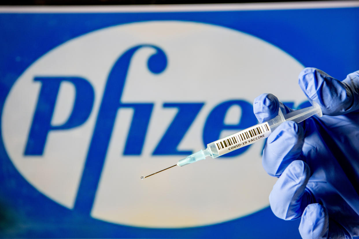 In this photo illustration, a man holds a syringe with a fake Covid-19 vaccine with the Pfizer logo in the background. Photo Illustration: Robin Utrecht/SOPA Images/LightRocket via Getty Images