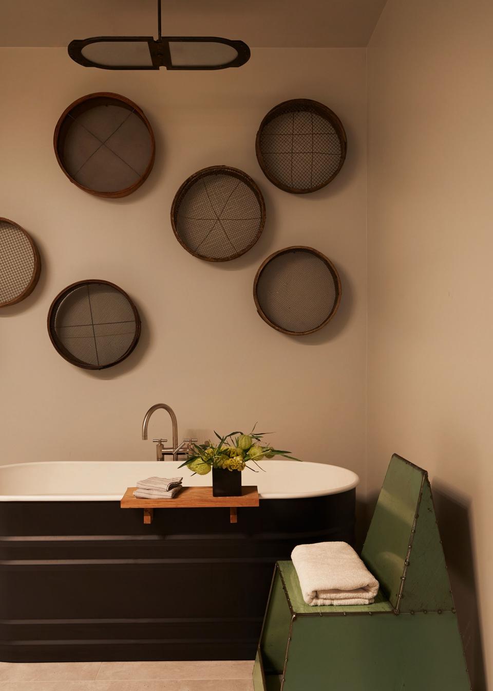 The matte finish of an Agape tub elevates the worn rusticity of a collection of vintage concrete sifters, which is complemented by the industrial edge of a metal chair in the master bath.