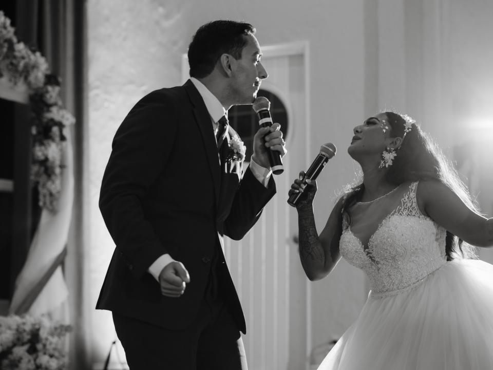 The bride and groom are holding microphones and singing to one another