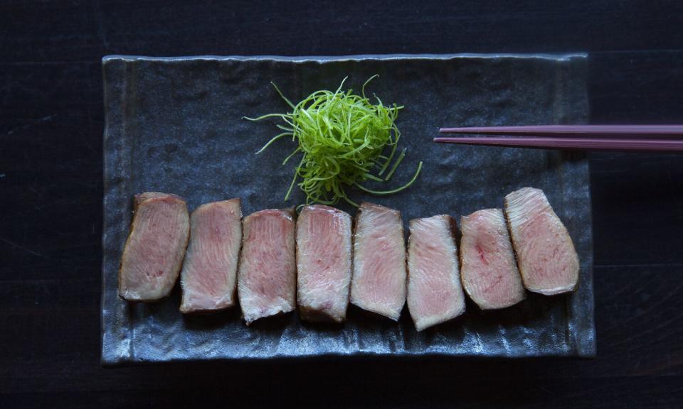 Eight slices of meat on a black ceramic plate, with a spiky green garnish and chopsticks.