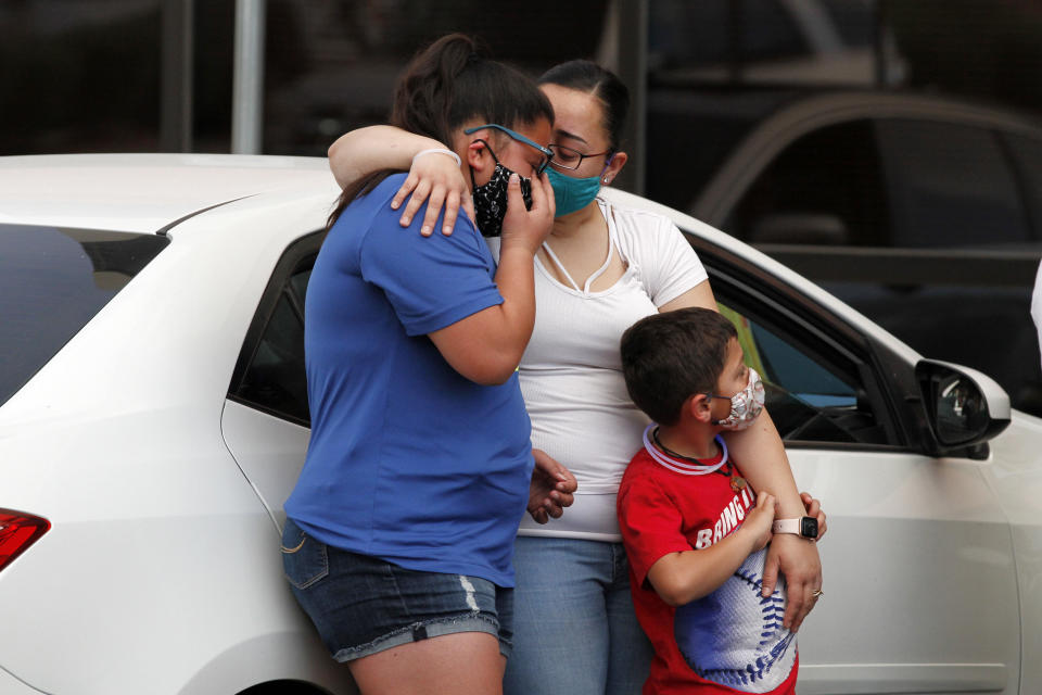 In this Thursday, May 21, 2020 photo, widow Jessica Coco Garcia, hugs her children at a memorial in the Del Sol Medical Center parking lot for father Guillermo "Memo" Garcia in El Paso, Texas. Memo Garcia died from bullet wounds he suffered in the Aug. 3 shooting at a Walmart after nine months in the hospital. Mourners wore masked and tried to stay apart to prevent the spread of COVID-19. (AP Photo/Cedar Attanasio)