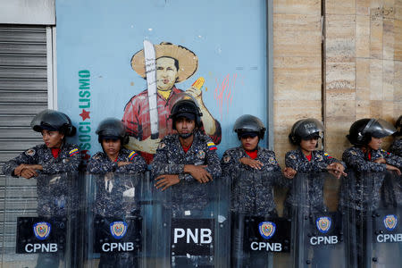 FILE PHOTO: Riot police officers stand in front of a mural depicting Venezuela's late President Hugo Chavez during a protest against Venezuela's president Nicolas Maduro's government, outside the building of the Labor Ministry in Caracas, Venezuela October 5, 2018. REUTERS/Carlos Garcia Rawlins/File Photo