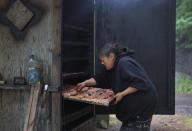 Sandy Whitefoot smokes salmon near the Bonneville Dam at an "in-lieu fishing site," lands set aside by Congress to compensate tribes whose villages were inundated by dams, on Monday, June 20, 2022. Many families at these sites live in trailers without restrooms, lights or drains. (AP Photo/Jessie Wardarski)